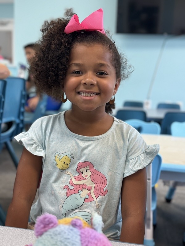 a little girl sitting at a table with a stuffed animal