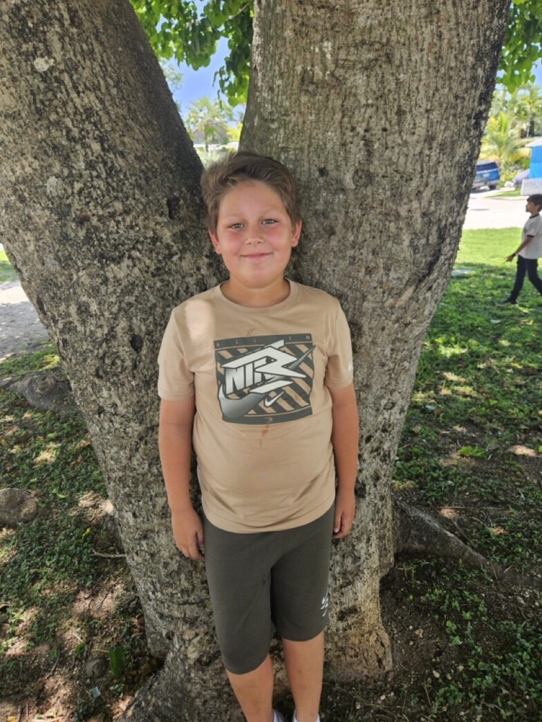 a young boy standing in front of a tree