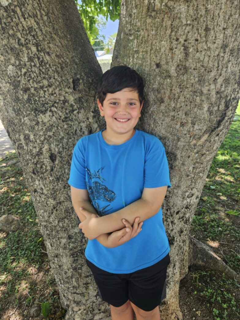 a young boy standing in front of a tree