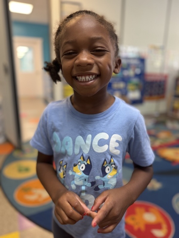 a young girl smiles while standing in a classroom