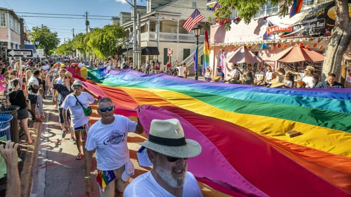 KeyWestPride_01_LarryBlackburn a group of people walking down a street holding a rainbow flag