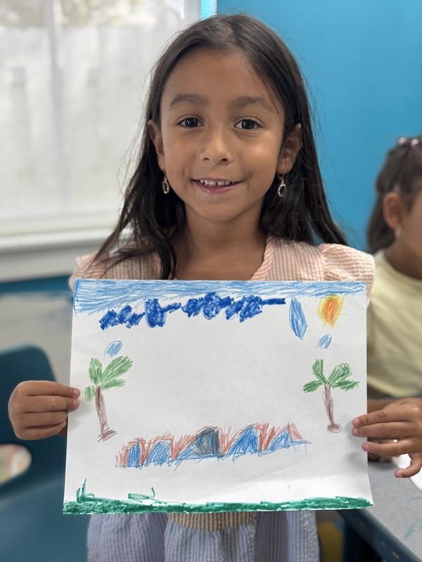 a young girl holding up a drawing in a classroom