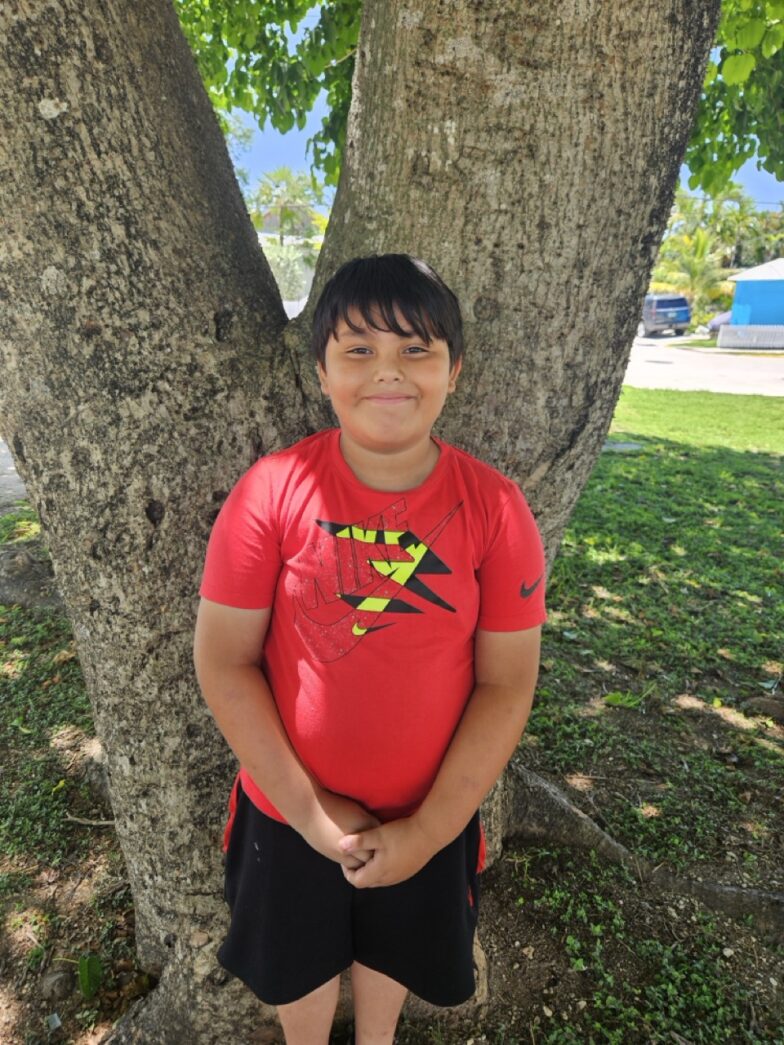 a young boy standing in front of a tree