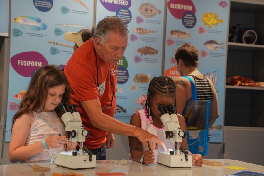 a man looking through a pair of microscopes at a young girl