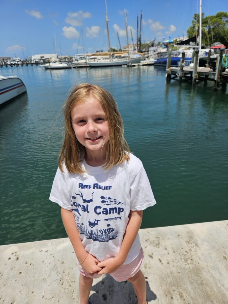 a little girl standing on a dock with a skateboard