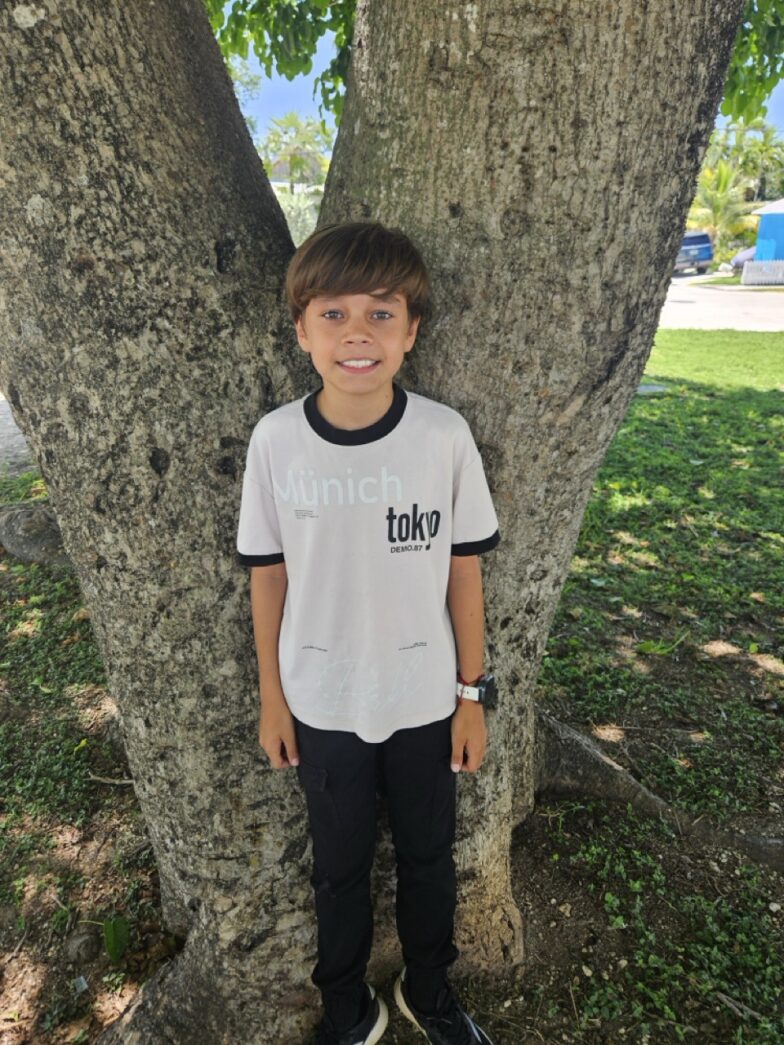 a young boy standing in front of a tree