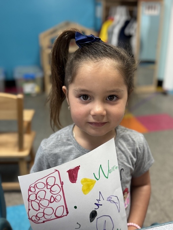 a little girl holding a piece of paper with drawings on it