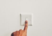 a hand pressing a light switch on a white wall
