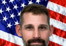 a man with a beard standing in front of an american flag