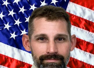 a man with a beard standing in front of an american flag