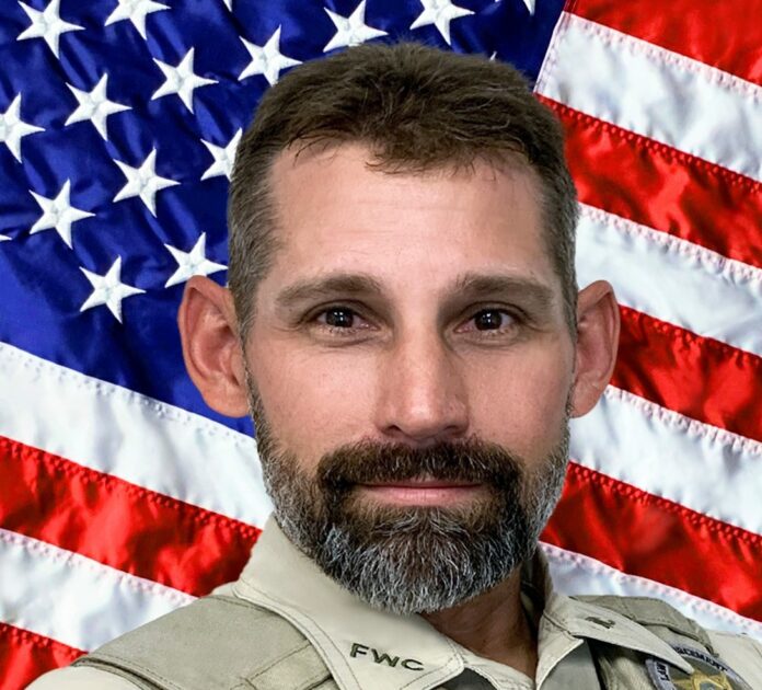 a man with a beard standing in front of an american flag
