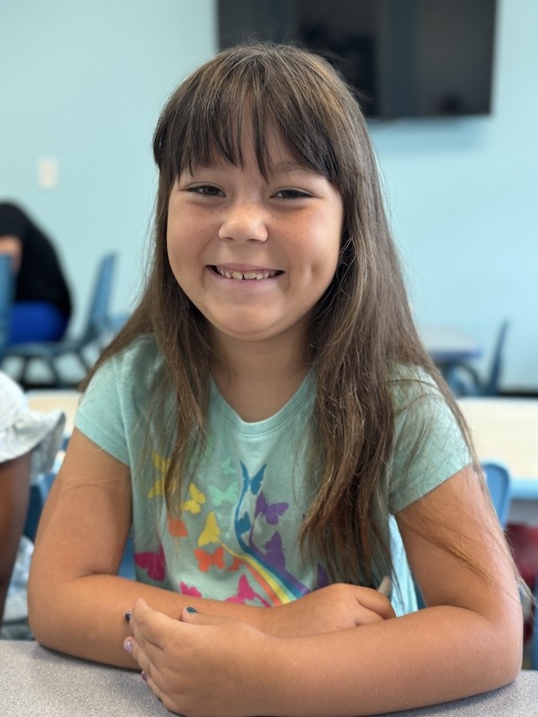 a young girl sitting at a table with her arms crossed