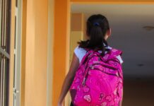 a young girl with a pink backpack walking down a hallway