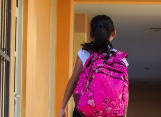 a young girl with a pink backpack walking down a hallway