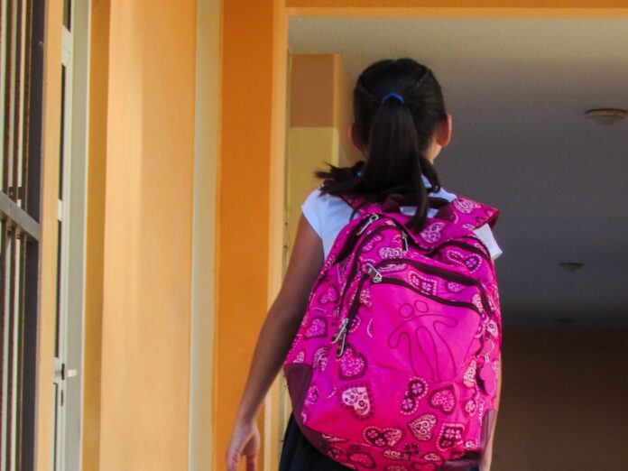 a young girl with a pink backpack walking down a hallway