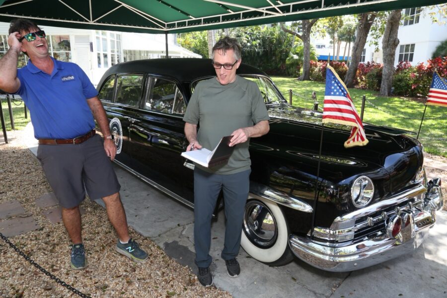 a man standing next to a black car under a tent