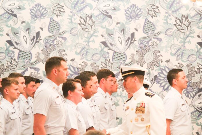 Rantuccio greets Coasties Large a group of men standing next to each other in front of a wall