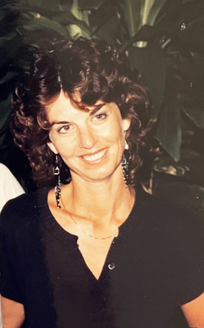 a woman smiling for a picture in front of a plant
