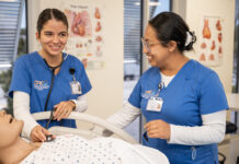 two women in scrubs standing around a dummy