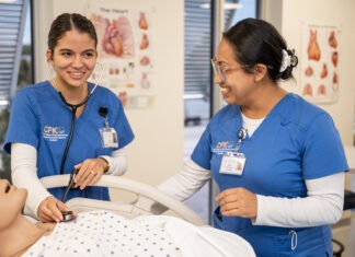two women in scrubs standing around a dummy