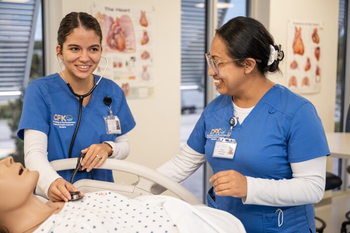 two women in scrubs standing around a dummy