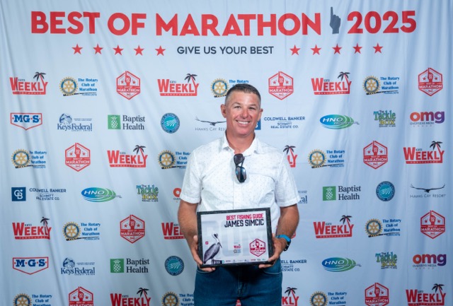 a man standing on a red carpet holding a plaque