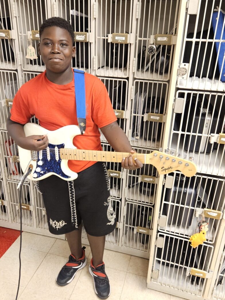 a young boy holding a guitar in front of a cage