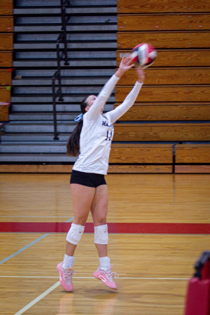 a girl jumps to hit a volleyball in a gym