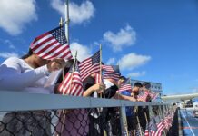 a group of people holding american flags behind a fence