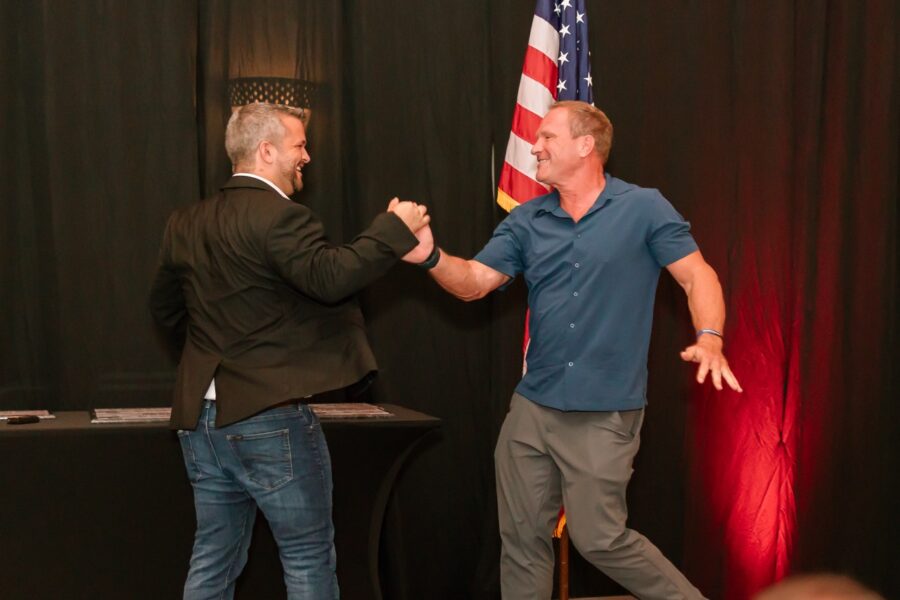 two men shaking hands in front of an american flag