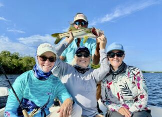 three people on a boat holding up a fish