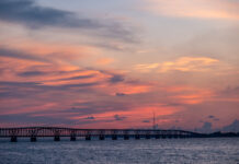 the sun sets over a bridge over water