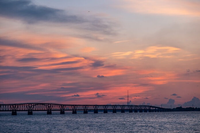 the sun sets over a bridge over water