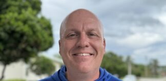 a man in a blue shirt standing in front of a lake