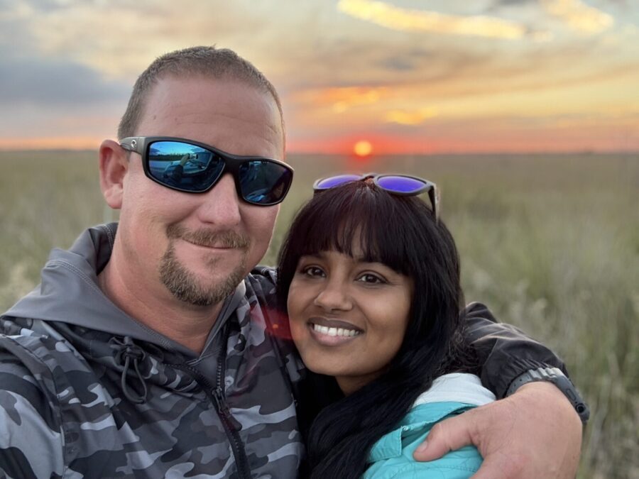 a man and a woman standing in a field at sunset