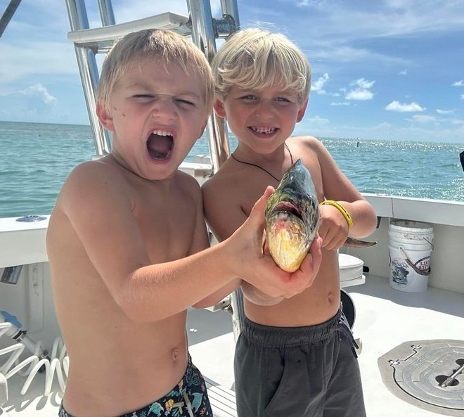two young boys holding a fish on a boat