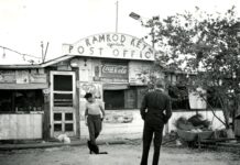 a black and white photo of a man and a woman walking in front of a