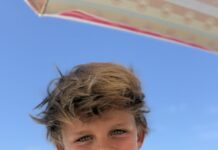 a young boy sitting under an umbrella on the beach