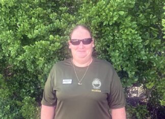 a woman in a green shirt standing in front of a bush