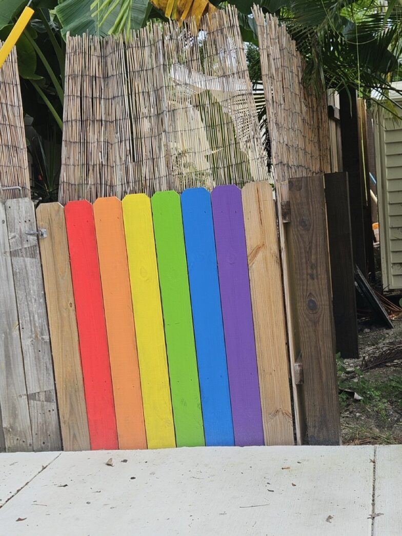 a rainbow colored fence with a banana tree in the background
