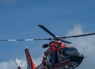 COAST GUARD RESCUES TWO PEOPLE AFTER THEIR KAYAK OVERTURNED OFF KEY LARGO a red helicopter flying through a cloudy blue sky