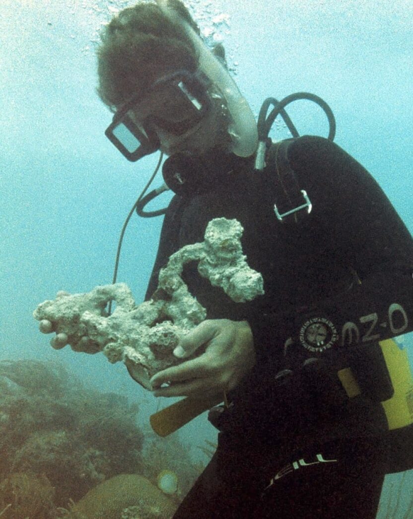 a man in a scuba suit holding a piece of coral
