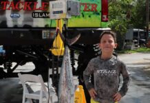 a young boy standing next to a boat holding a fish