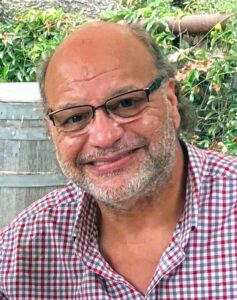 a man with a beard and glasses sitting in front of a barrel