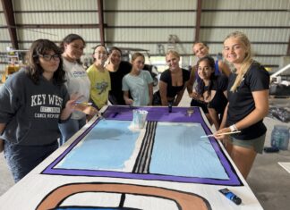 a group of people standing around a table with a painting on it
