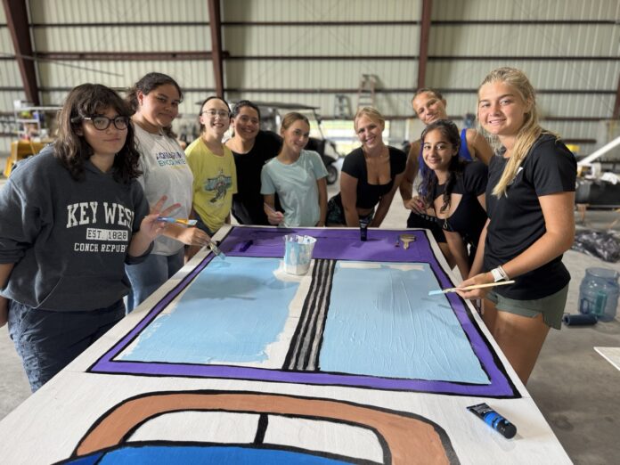 a group of people standing around a table with a painting on it