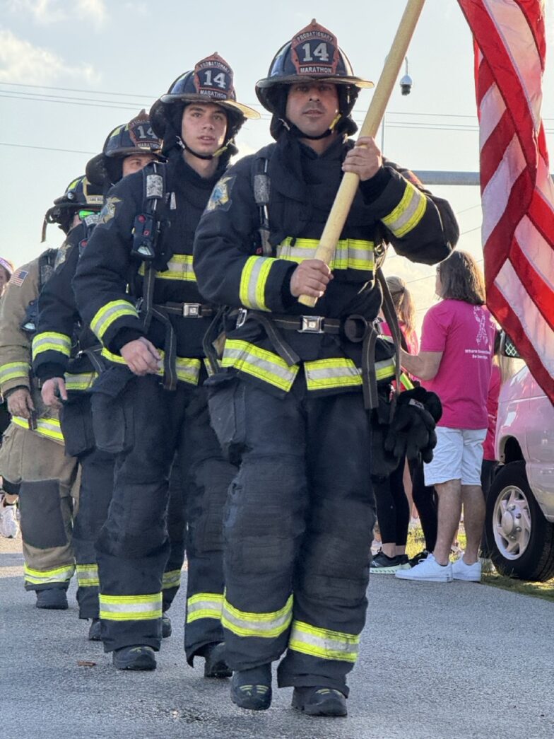 a group of firemen walking down a street holding a flag
