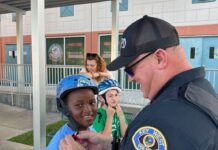 OFF TO THE RACES: COPS CLOCK 5TH GRADE SPEEDSTERS AT PELICANS & POLICE EVENT a police officer helping a young boy put on his helmet