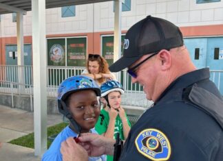 OFF TO THE RACES: COPS CLOCK 5TH GRADE SPEEDSTERS AT PELICANS & POLICE EVENT a police officer helping a young boy put on his helmet