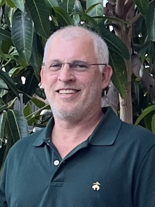 a man in a green shirt standing in front of a tree